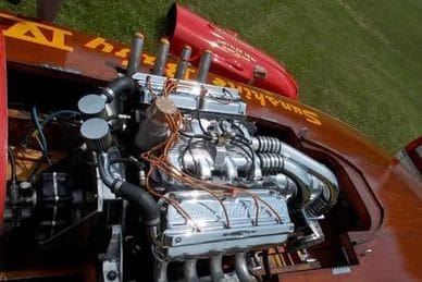 Close-up of a vintage car engine with chrome details and visible wiring, set against a green grass background.