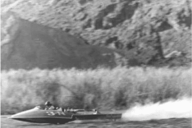 A speedboat racing along a river with a mountainous background and a trail of water spray behind.